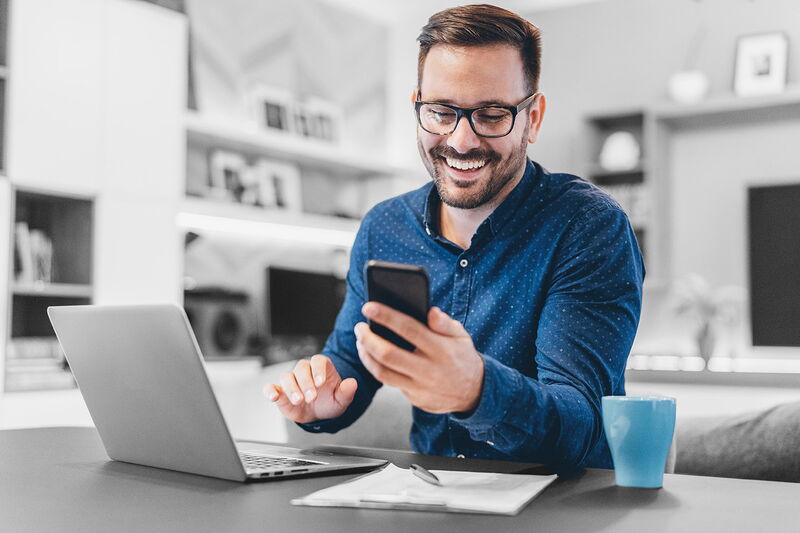Mitarbeiter sitzt motiviert am Laptop und Handy